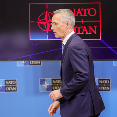 Jens Stoltenberg i profil framför Natos logotyp på en skärm.