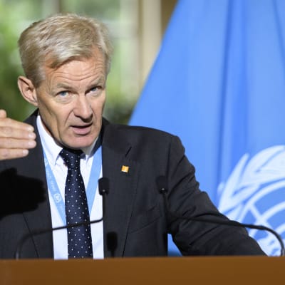 Jan egeland, chef för det humanitära arbetet i Syrien, gestikulerar och talar framför FN:s flagga. 