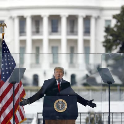 Donald Trump puhujakorokkeella Valkoinen talo taustallaan