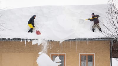 Två män skottar snö från ett tak i Filzmoos i Österrike. Flera byggnader i landet har kollapsat av snömassorna.