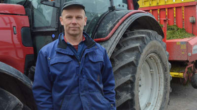 En man, bonde, står framför sin traktor.