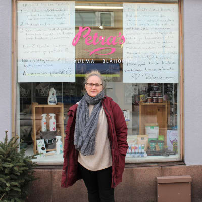 Kvinna utanför affär med stora handskrivna skyltar i fönstret
