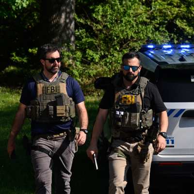 Två beväpnade män i FBI-västar står vid en polisbil.