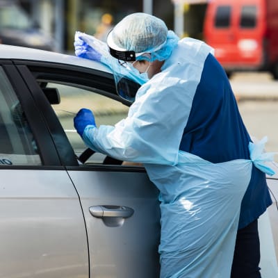 En vårdare i skyddsutrustning tar coronatest på en person i en bil.