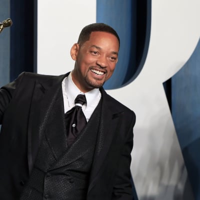 Will Smith klädd i kostym ler medan han poserar med sin Oscarsstatyett på röda mattan.