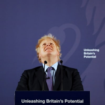 Boris Johnson står framför en blå bakgrund och tittar leende upp i luften.