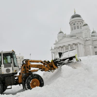 En snöplog lassar snö i en stor snöhög på Senatstorget framför Domkyrkan i Helsingfors under Valtteri-snöstormen.