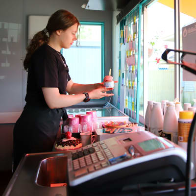 En glassförsäljare inne i en glasskiosk räcker ut en glass åt en kund som står utanför.