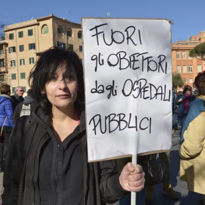 Demonstrant med skylt på italienska i Rom där det står: Ut med samvetsvägrarna från de offentliga sjukhusen