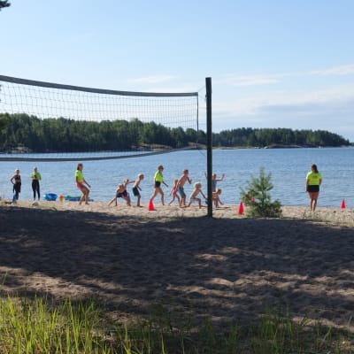 Simskoledeltagare leker på stranden med en volleybollsplan i förgrunden.