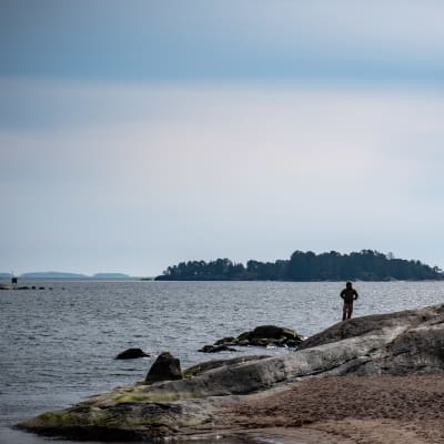 Mies seisoo rantakalliolla Aurinkolahden rannalla.