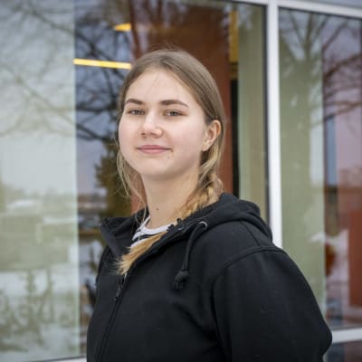 17-vuotias Aada Huhtala katsoo kameraan ja hymyilee. Huhtalalla on lettikampaus ja musta huppari. 