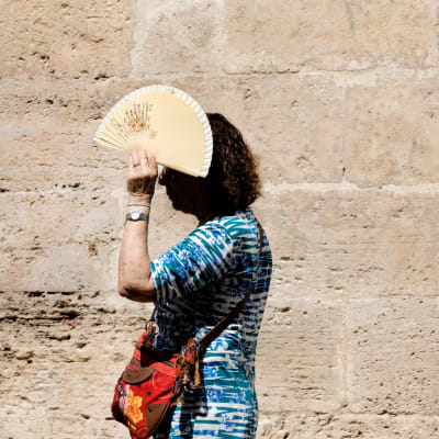 Nainen pitää viuhkaa kasvojensa edessä suojautuakseen auringolta.