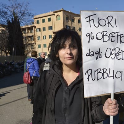 Demonstrant med skylt på italienska i Rom där det står: Ut med samvetsvägrarna från de offentliga sjukhusen