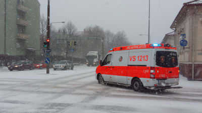En ambulans på utryckning svänger runt ett gathörn på snöiga gator.