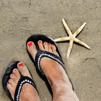 kvinnliga fötter nergrävda i sanden, brevid fötterna finns en stjärnformad snäcka.  