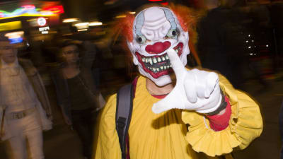 En person utklädd till en skrämmnade clown. Gul dräkt, rött hår och förvridet ansikte.