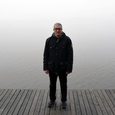 professor tommi lehtonen står på en brygga med ett dimmigt hav bakom sig. Han bär mörka kläder. 