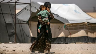 En kvinna bär på ett litet barn inne i lägret al-Hol 2.6.2019.