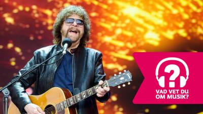 Jeff Lynne spelar akustisk gitarr och sjunger i en mikrofon som är i en mikrofonställning.