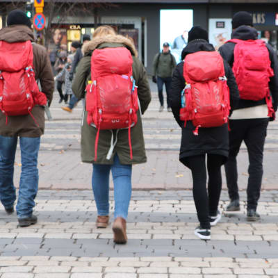fyra personer med röda ryggsäckar går över vägen.