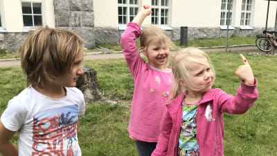 Flicka håller upp nyckelpiga på sitt pekfinger, två andra barn ser på.
