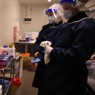 Två sjukskötare i skyddsutrustning står vid en coronatestningsstation.