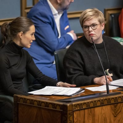 Marin och Saarikko ser buttert på varann i regeringsbåset i riksdagen.