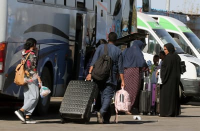 Människor går med kassar och kappsäckar mot en buss som har baggageluckan öppen.