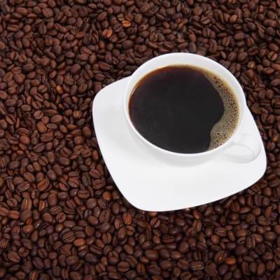 En kaffekopp med kaffe i står på en bädd med kaffebönor.