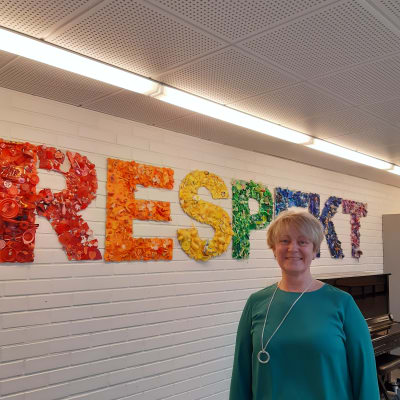 Rektor Catharina Sunesdotter står framför en bild med texten respekt i skolans korridor.
