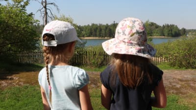 Två flickor iklädda hatt och keps står och blickar ut över havet vid daghemmet Tallbo.