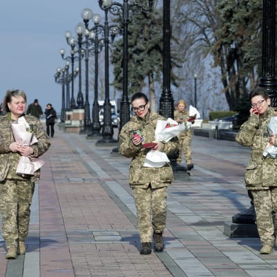 Tre kvinnor i soldatuniformer går med blommor i händerna.