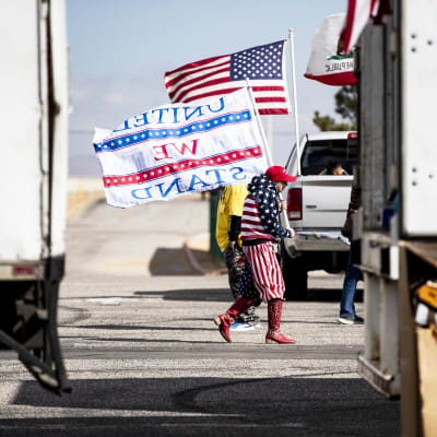 Yhdysvaltain lipun väreihin ja kuvioihin pukeutunut henkilö kantaa lippua rekkojen edustalla.