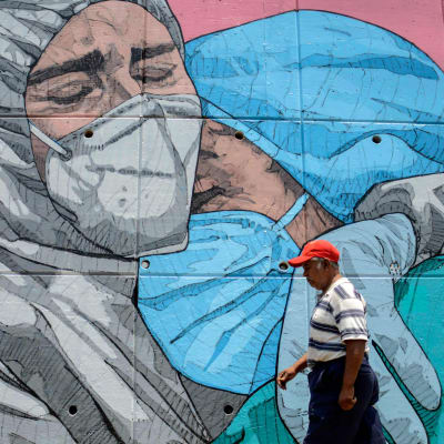 En man går förbi en väggmålning av två sjukskötare som kramar varandra i Mexiko.