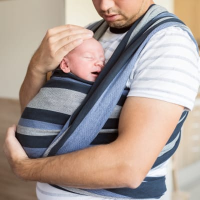 En pappa vars ansikte inte syns håller ett barn mot sitt bröst.