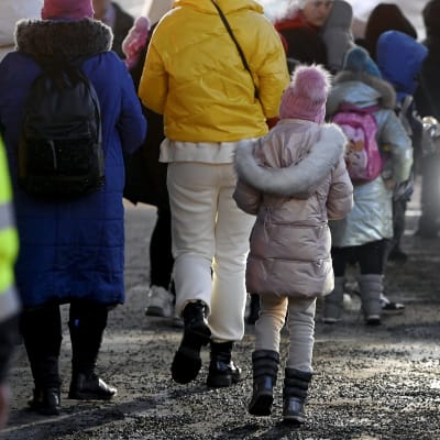 Ukrainska flyktingar i vinterklädsel promenerar med ryggen mot kameran på Busholmen i Helsingfors den 16 mars 2022.