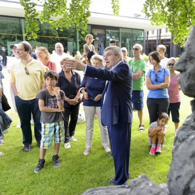 KOK:n johtaja Thomas Bach vieraineen Pierre de Coubertinin patsaalla Sveitsin Lausannessa.