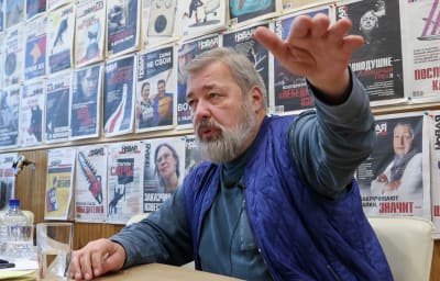 Dmitri Muratov sitter framför en vägg som är täckt med förstasidor av tidningar och gestikulerar när han pratar.