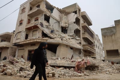 Två män går förbi en svårt skadad byggnad efter en jordbävning i staden Zardana i Syrien.