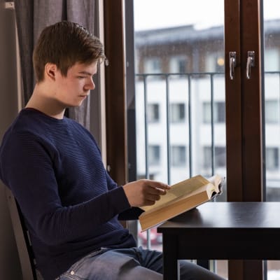 Opiskelija Mikko Vanhala lukee oppikirjaa ikkunan edessä omassa vuokrayksiössään.