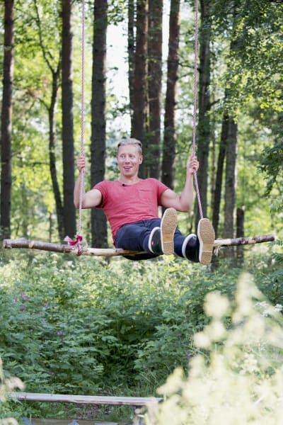 Toimittaja Nicke Aldén puuhun ripustetussa keinussa Varjakansaaressa Oulussa, taustalla kesäinen metsä.
