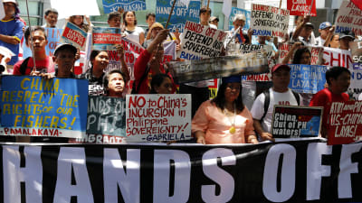 Filippinier står med plakat utanför Kinas konsulat i Makati, Filippinerna. På plakaten står olika texter mot Kinas territoriella krav på bland annat ögruppen Spratly i Sydkinesiska havet.