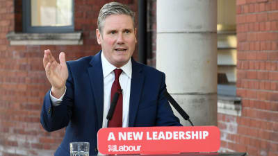 En kostymbeklädd Keir Starmer står bakom ett podium där det står "A ned leadership - labour".