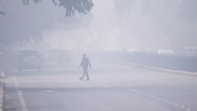 En man korsar en gata i New Delhi 4.11.2019. Hostande människor försökte skydda sig mot svidande smog, skolor stängdes, bilar förbjöds att köra och byggverksamheten avstannade.