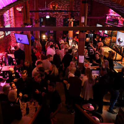 Stor mängd människor socialiserar sig vid en bar. Bilden är tagen uppifrån.