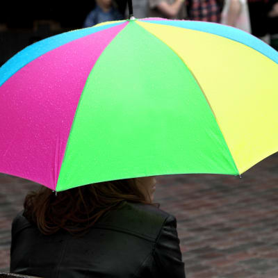 En person håller i ett paraply med ljusblå, lila, grön och gul färg.