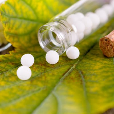 vita piller och en pillerburk av glas på ett grönt löv