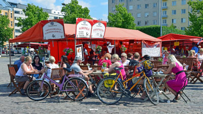 Människor sitter vid ett kafé på ett torg. Det är sommar. 