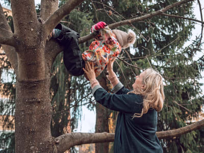 Äiti pitelee kiinni lapsesta, joka kiipeilee puussa.